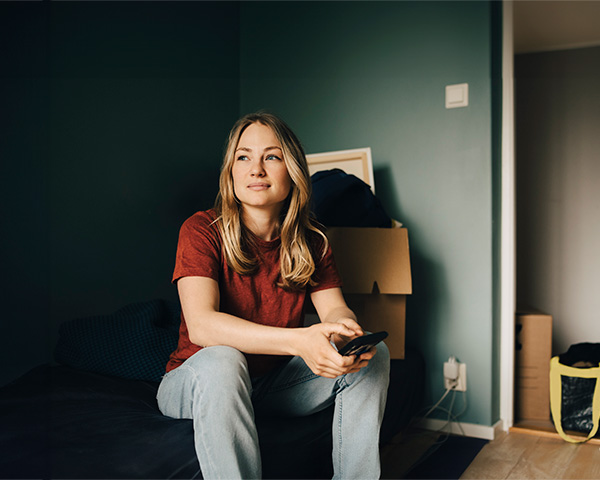 Thoughtful young woman looking away while sitting in an empty room with moving boxes around her 