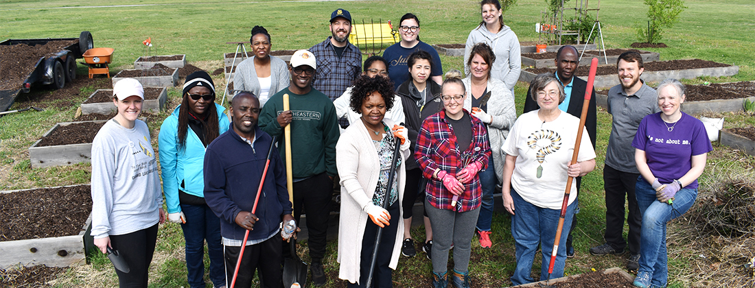 Group of volunteers pose with gardening tools at community garden