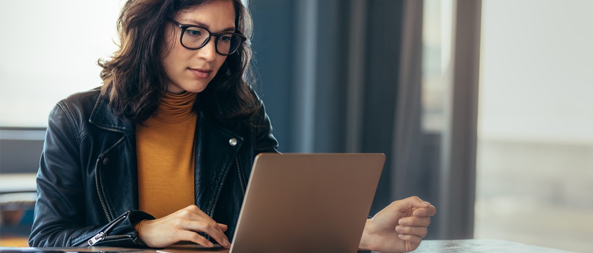 A young woman wear glasses and a leather jacket looking at a laptop