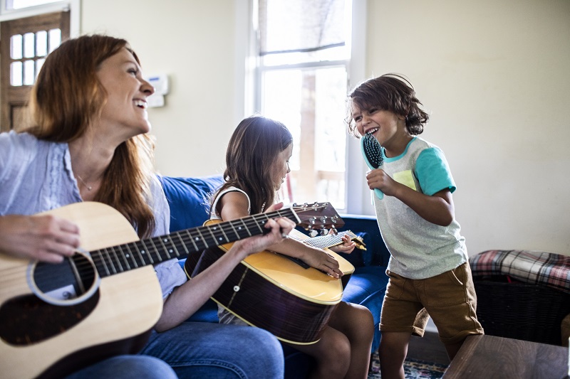 Madre e hija tocando la guitarra mientras el hijo canta con un cepillo para el pelo
