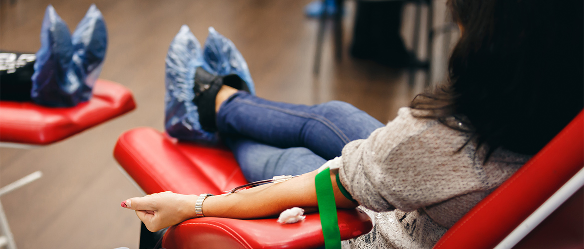Woman sits in red chair with left arm hanging over while giving blood