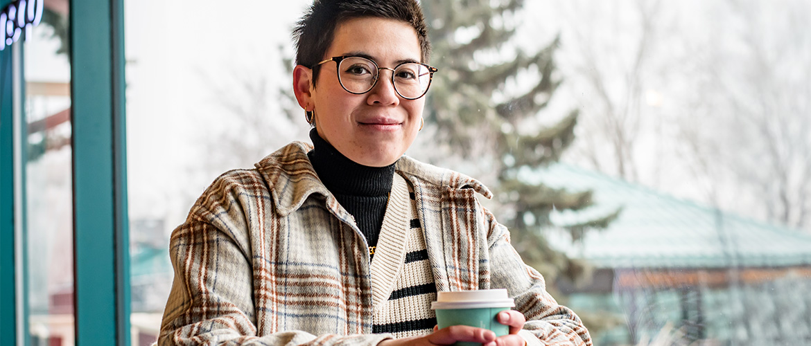 Woman holds coffee cup while sitting in front of window