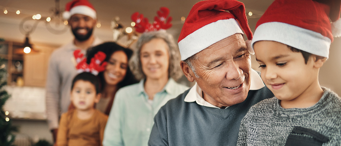 Family wearing Santa hats gathers as older man plays a keyboard while holding a boy on his knee