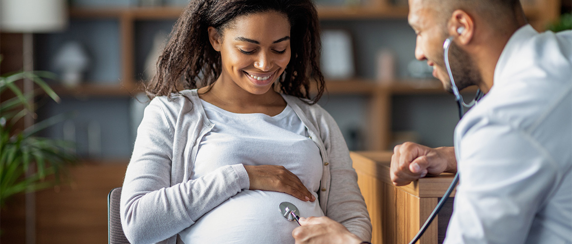 A health care provider holds a stethoscope to a pregnant woman's abdomen