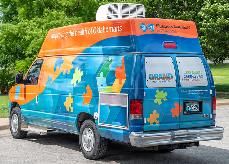 exterior rear view of a van with orange and blue wrap with logos of Grand Mental Health and Oklahoma Caring Van Program