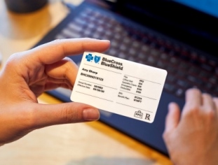 Woman's hand holding a BCBS ID card while on her laptop.