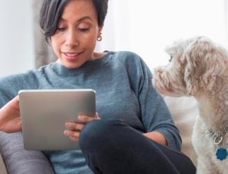 Mujer sentada en un sofá con su perro trabajando en una tableta.