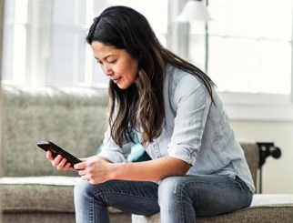 Mujer sentada en un banco en la sala de estar de su casa, mirando su teléfono móvil como si estuviera esperando un mensaje.