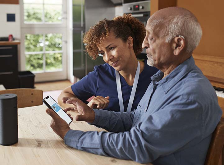 Younger woman helping elderly man on his smart phone.