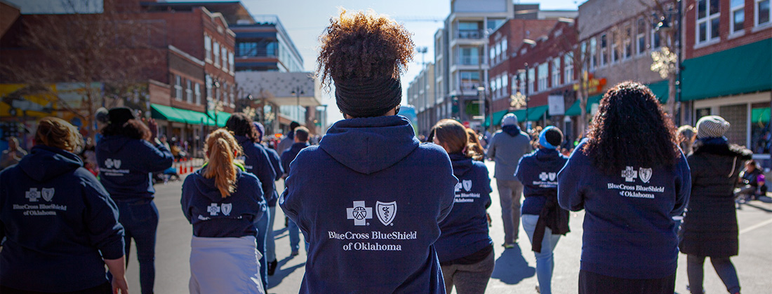 Women in BCBSOK sweatshirts march together along building-lined street