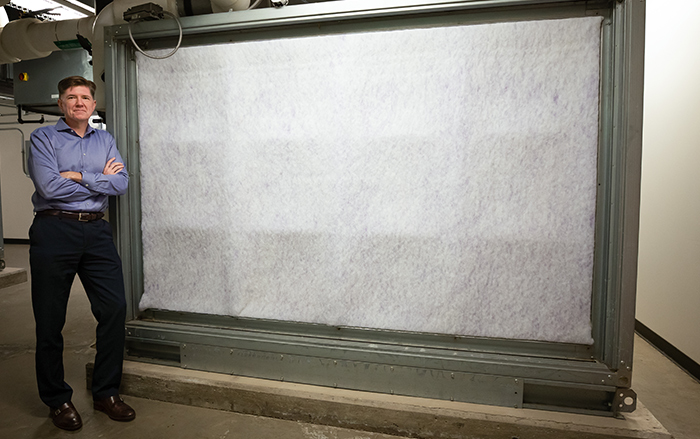 Man stands next to very large air filter.