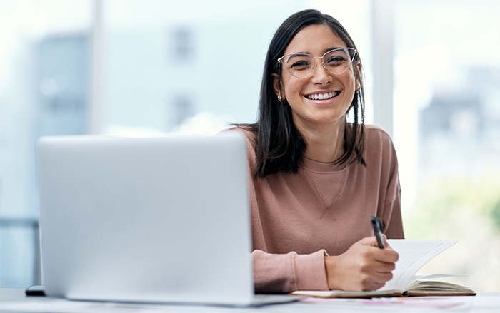 Woman with glasses smiles from behind computer