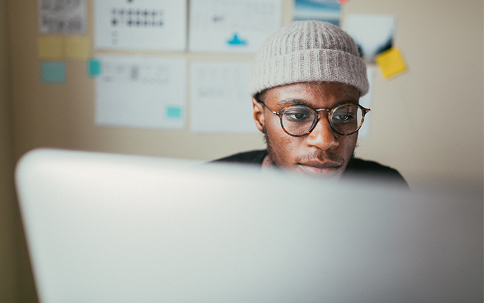 Black man wearing beanie looks at computer intently