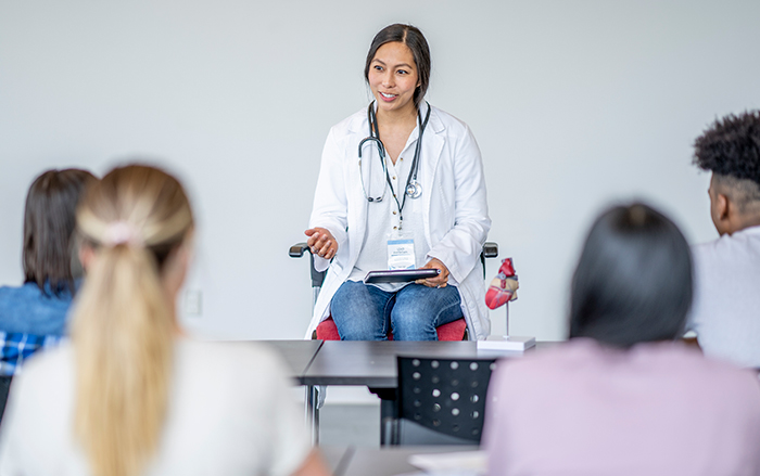 Una profesional de la salud sentada delante de la clase hablando con los alumnos