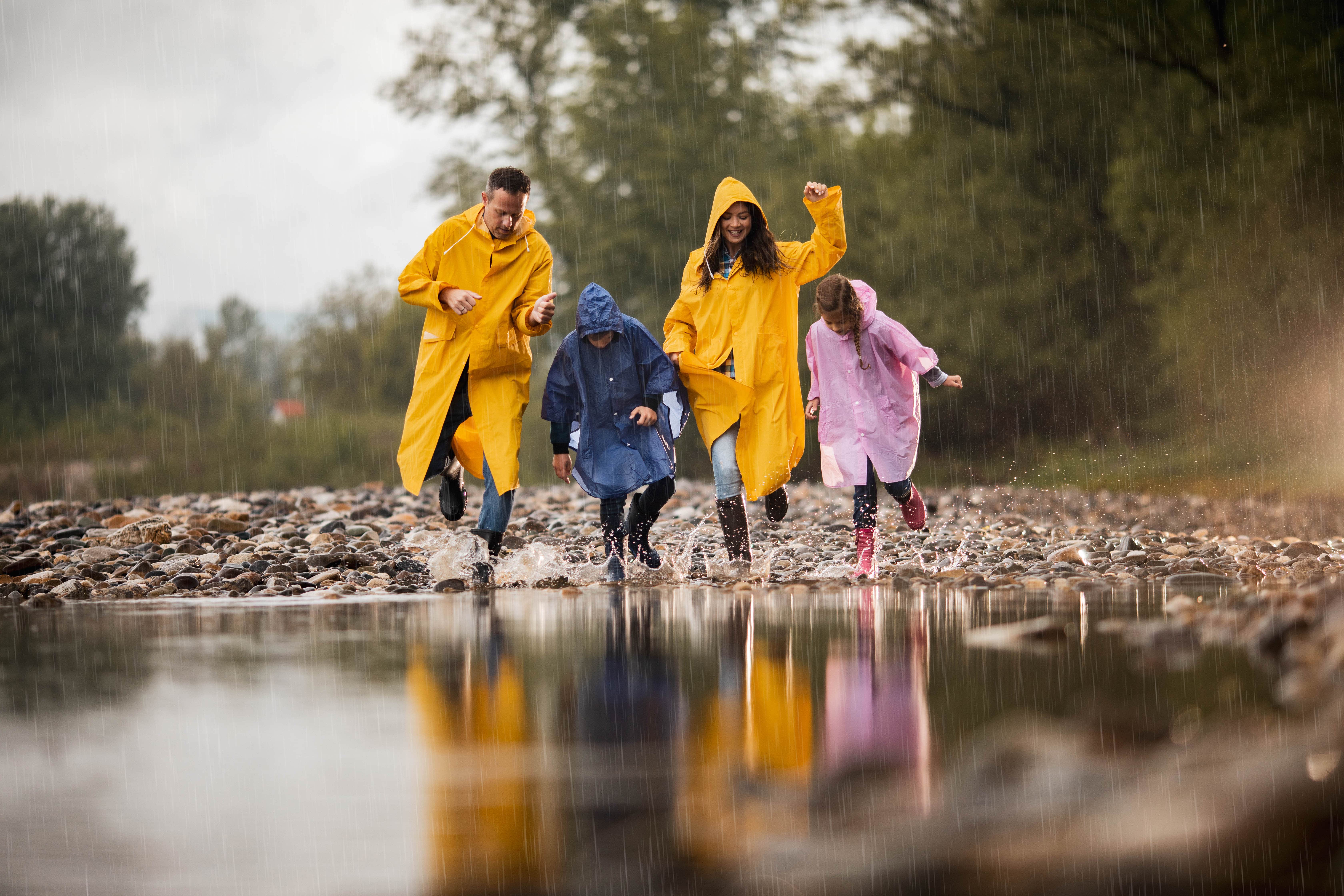 Familia con botas de lluvia e impermeables bailando alrededor de un gran charco