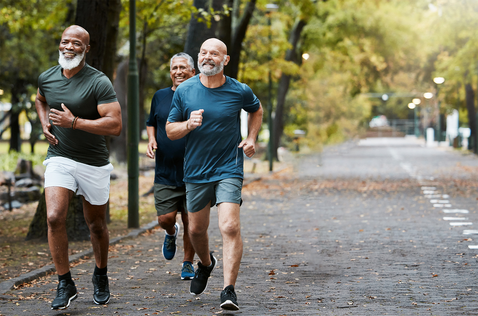 Senior men running smiling as they run through the park.