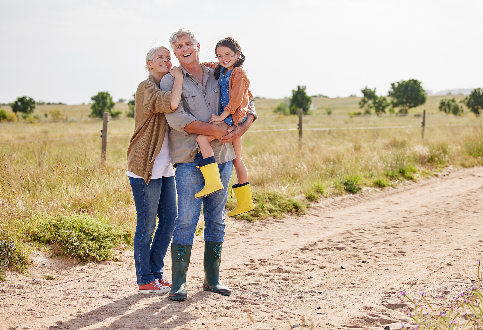 Senior man and woman pose on a dirt road. The man carring his granddaughter. 